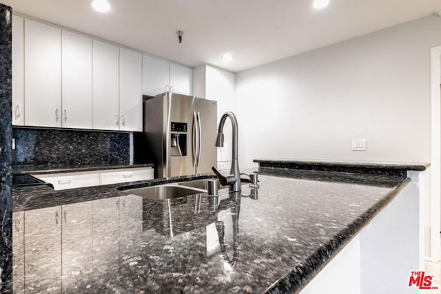 kitchen featuring white cabinetry, tasteful backsplash, stainless steel refrigerator with ice dispenser, kitchen peninsula, and dark stone counters