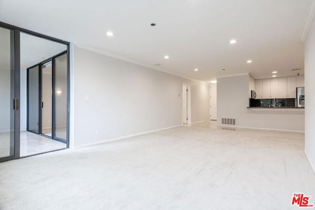 unfurnished living room with light colored carpet, crown molding, and sink