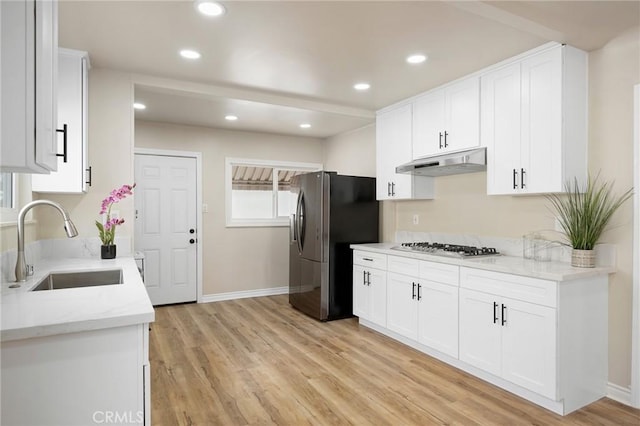 kitchen with under cabinet range hood, stainless steel appliances, a sink, white cabinetry, and light wood-type flooring