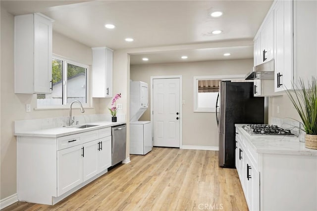 kitchen with light wood-style flooring, stainless steel appliances, a sink, light countertops, and stacked washer and clothes dryer