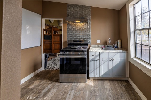 kitchen featuring lofted ceiling, sink, stainless steel gas stove, range hood, and dark hardwood / wood-style flooring