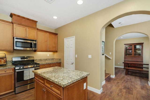 kitchen with light stone countertops, dark wood-type flooring, stainless steel appliances, and a center island