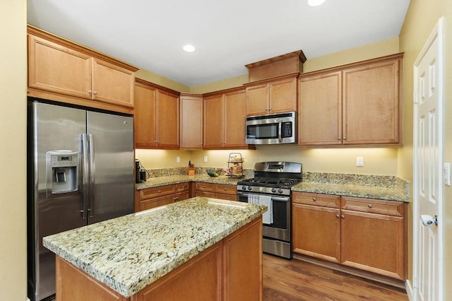 kitchen featuring stainless steel appliances, wood-type flooring, a kitchen island, and light stone counters