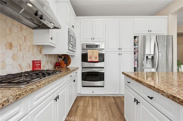 kitchen featuring appliances with stainless steel finishes, white cabinetry, light stone counters, custom range hood, and light wood-type flooring