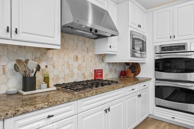 kitchen with white cabinetry, stainless steel appliances, backsplash, and dark stone countertops