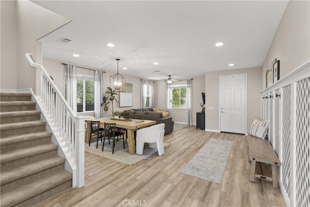 dining space with ceiling fan with notable chandelier and light hardwood / wood-style floors