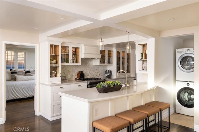 kitchen with stacked washer / dryer, stainless steel gas stove, white cabinets, and dark hardwood / wood-style floors