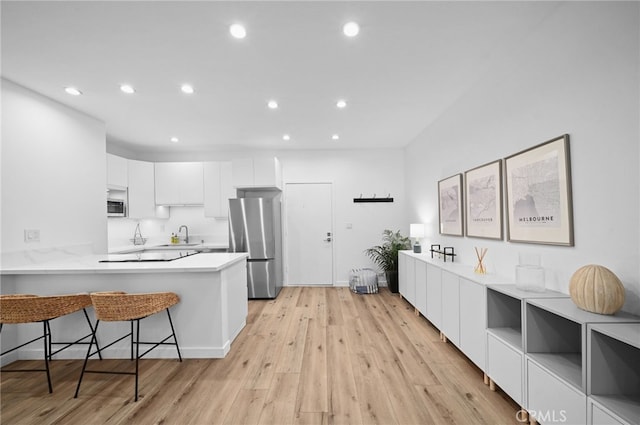 kitchen featuring appliances with stainless steel finishes, a kitchen breakfast bar, white cabinets, kitchen peninsula, and light wood-type flooring