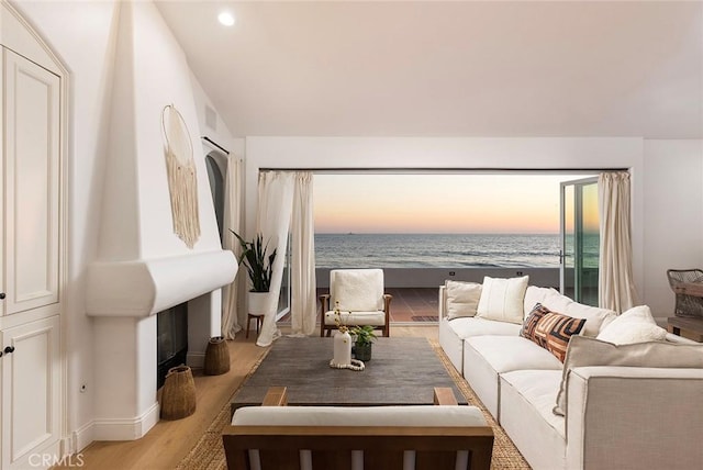 living room featuring a beach view, light wood-type flooring, and a water view