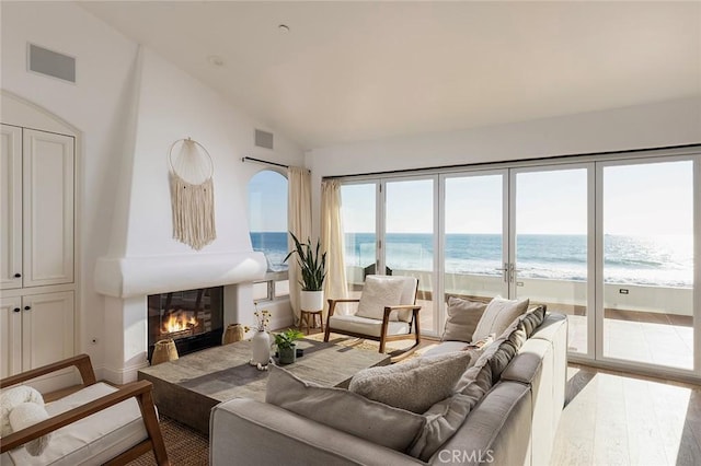 living room with vaulted ceiling, hardwood / wood-style floors, a water view, and a view of the beach