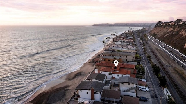 aerial view at dusk featuring a water view and a view of the beach