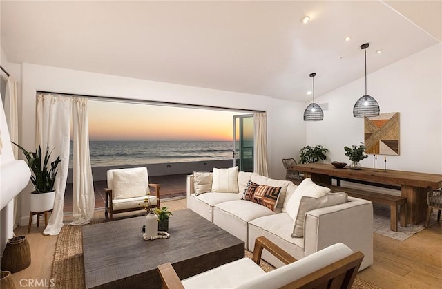 living room with a view of the beach, vaulted ceiling, a water view, and light hardwood / wood-style flooring