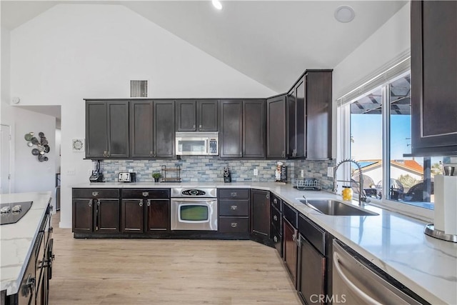 kitchen featuring appliances with stainless steel finishes, high vaulted ceiling, tasteful backsplash, and sink