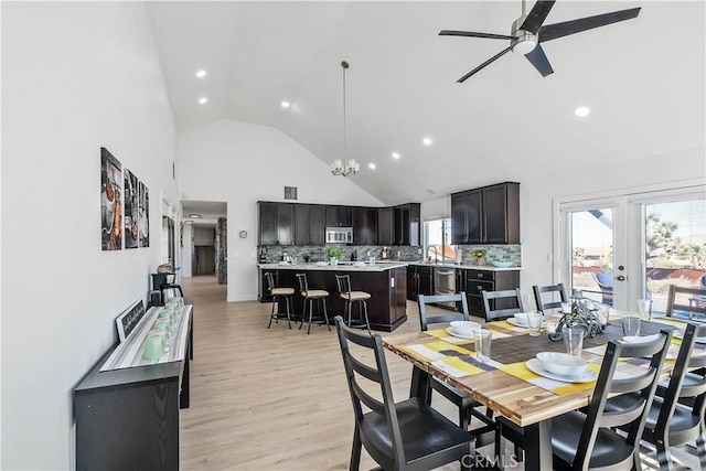 dining room with ceiling fan with notable chandelier, french doors, sink, high vaulted ceiling, and light hardwood / wood-style flooring