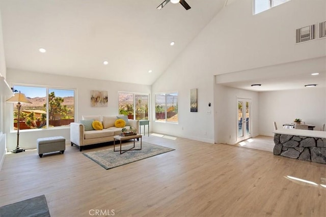 living room with ceiling fan, a towering ceiling, and light wood-type flooring