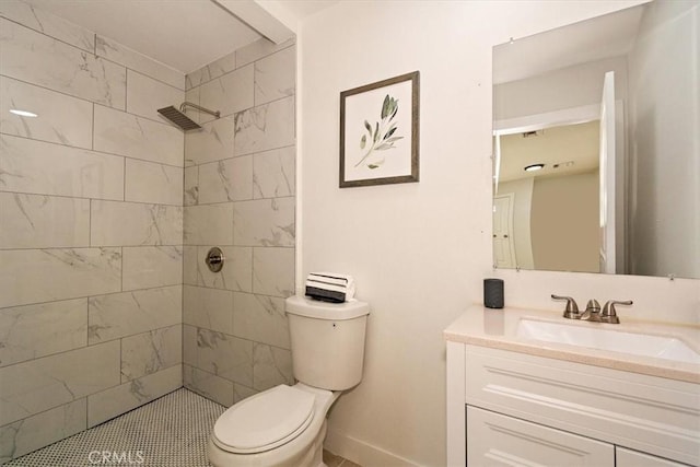 bathroom with toilet, a tile shower, and vanity