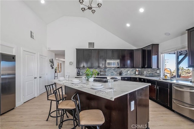 kitchen with a center island, light stone countertops, stainless steel appliances, high vaulted ceiling, and dark brown cabinets