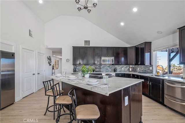 kitchen featuring a kitchen island, dark brown cabinetry, appliances with stainless steel finishes, high vaulted ceiling, and light stone counters