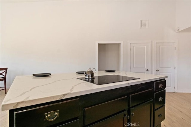 kitchen featuring light stone counters, light hardwood / wood-style flooring, black electric cooktop, and a kitchen island