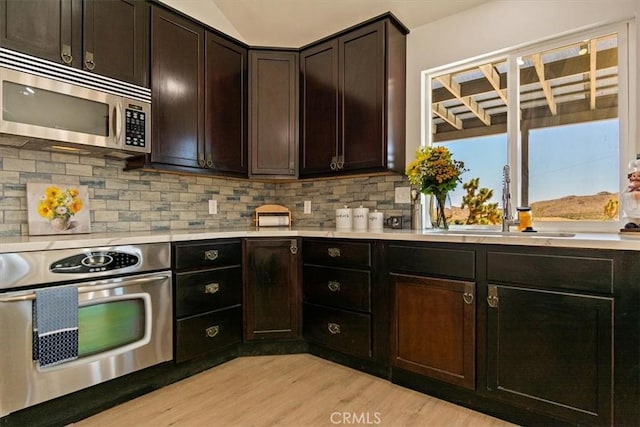 kitchen featuring appliances with stainless steel finishes, sink, backsplash, light hardwood / wood-style flooring, and dark brown cabinets