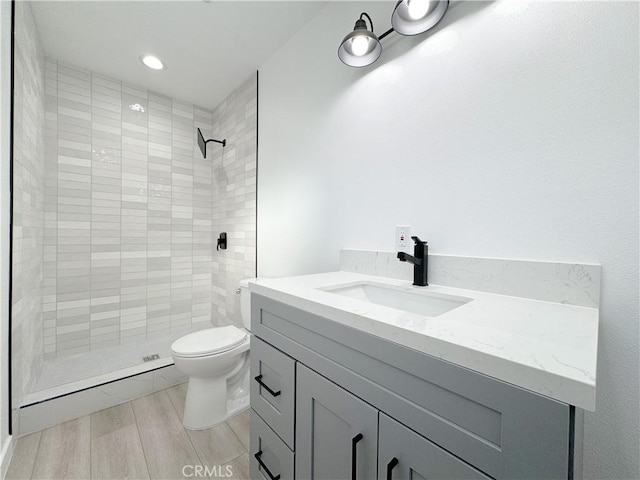 bathroom with vanity, toilet, wood-type flooring, and a tile shower