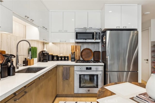 kitchen featuring decorative backsplash, white cabinetry, sink, and appliances with stainless steel finishes