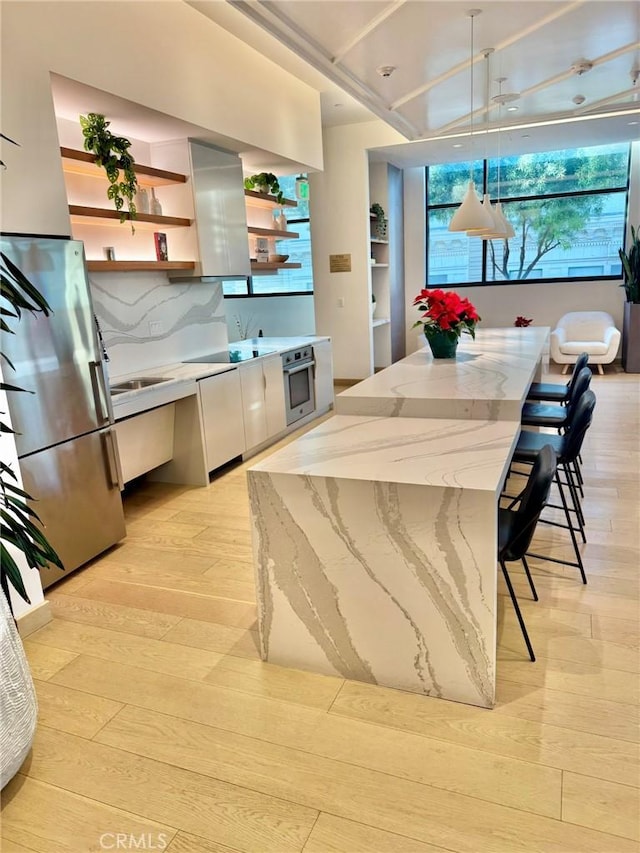 kitchen with ventilation hood, light stone countertops, light wood-type flooring, decorative light fixtures, and stainless steel appliances