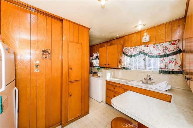 kitchen featuring washer / clothes dryer, wooden walls, sink, and white fridge