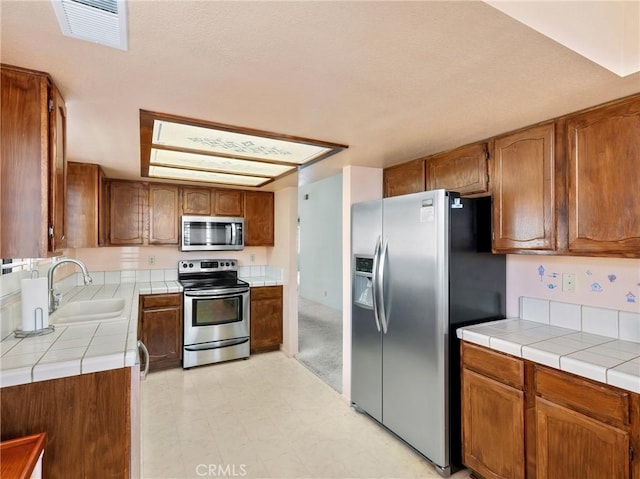 kitchen with tile counters, sink, and appliances with stainless steel finishes