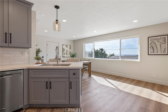 kitchen featuring gray cabinetry, sink, stainless steel dishwasher, backsplash, and hardwood / wood-style floors