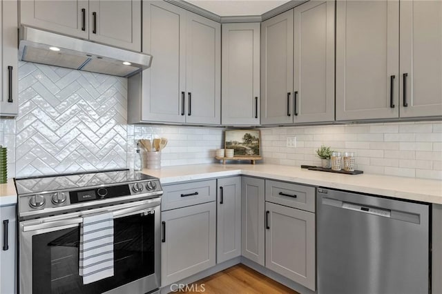 kitchen with backsplash, stainless steel appliances, light hardwood / wood-style flooring, and gray cabinetry