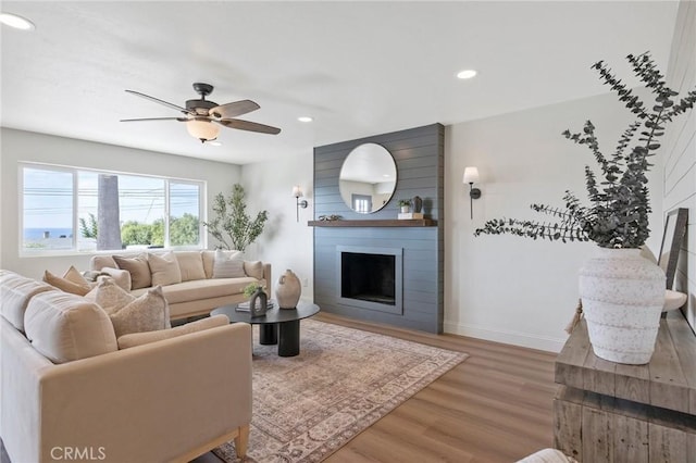 living room featuring wood-type flooring, a large fireplace, and ceiling fan