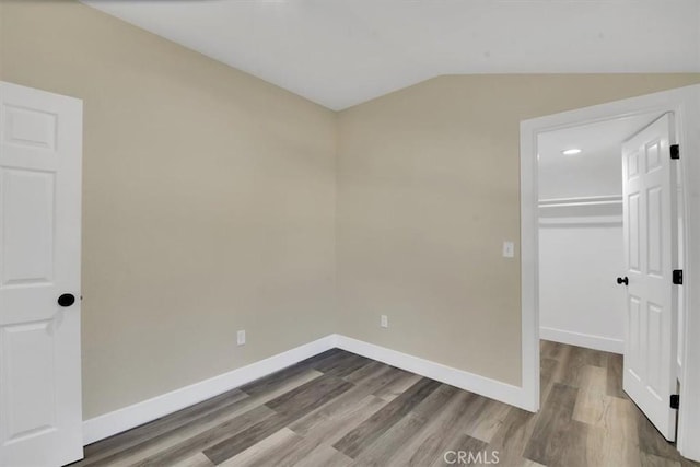 unfurnished bedroom with hardwood / wood-style flooring, a closet, a spacious closet, and vaulted ceiling