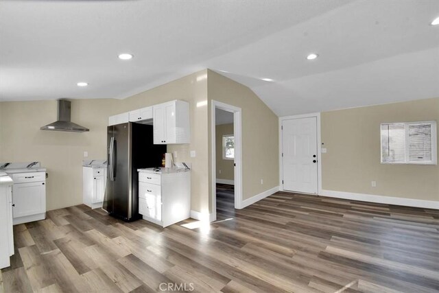 kitchen featuring lofted ceiling, wall chimney range hood, stainless steel refrigerator with ice dispenser, light hardwood / wood-style flooring, and white cabinetry