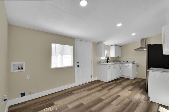 kitchen with sink, wall chimney exhaust hood, light hardwood / wood-style floors, black refrigerator, and white cabinets