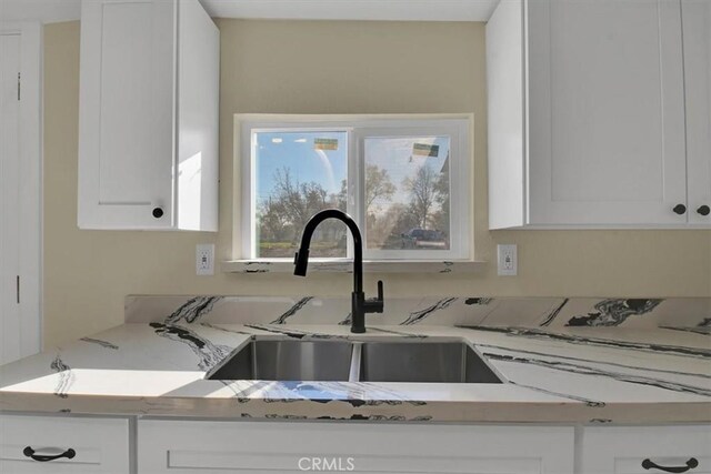 kitchen with light stone counters, white cabinetry, and sink