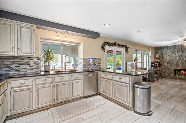 kitchen with kitchen peninsula, tasteful backsplash, sink, dishwasher, and a fireplace