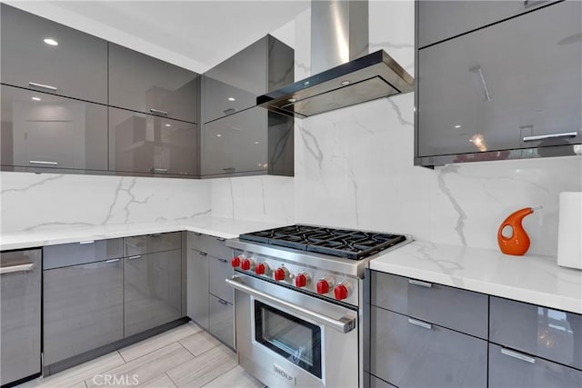 kitchen featuring decorative backsplash, appliances with stainless steel finishes, wall chimney range hood, and light stone counters