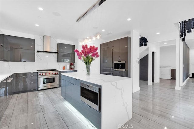 kitchen with high end appliances, a kitchen island, decorative light fixtures, and wall chimney range hood