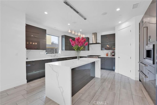 kitchen featuring decorative backsplash, decorative light fixtures, a kitchen breakfast bar, a kitchen island with sink, and wall chimney exhaust hood