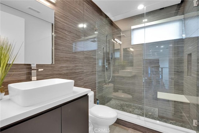 bathroom featuring toilet, vanity, tile walls, and a shower with shower door