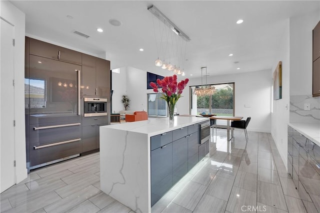 kitchen with pendant lighting, tasteful backsplash, a large island, a notable chandelier, and light stone counters