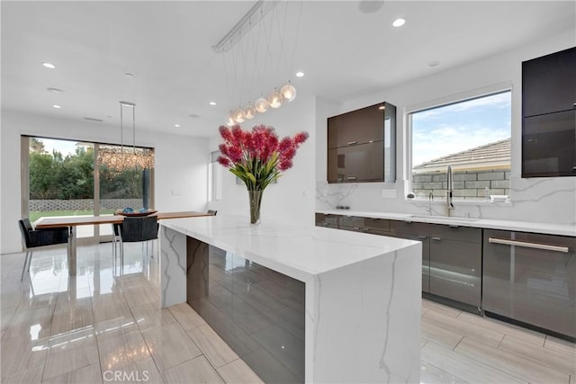 kitchen featuring decorative light fixtures, sink, dishwasher, light stone counters, and a center island