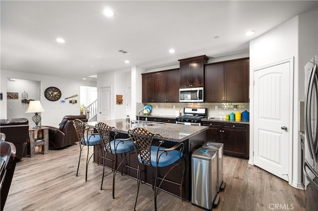 kitchen with sink, dark brown cabinets, appliances with stainless steel finishes, a kitchen breakfast bar, and an island with sink