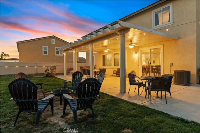 patio terrace at dusk with ceiling fan, an outdoor fire pit, a yard, and central air condition unit