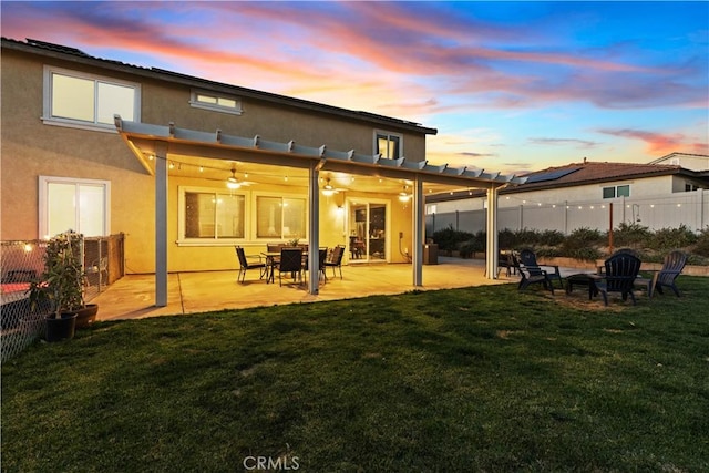 back house at dusk featuring a patio area, ceiling fan, and a lawn