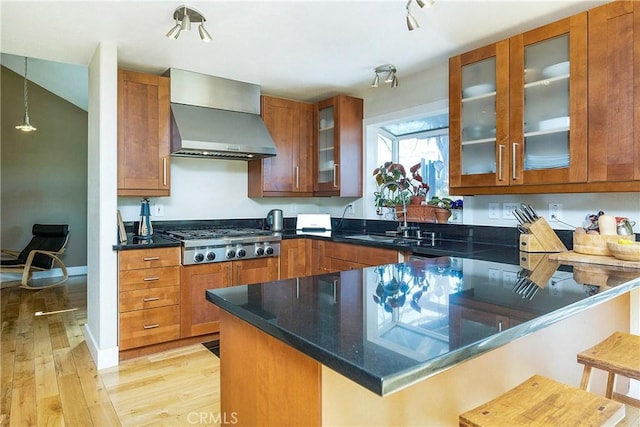 kitchen with kitchen peninsula, a kitchen breakfast bar, wall chimney exhaust hood, light hardwood / wood-style flooring, and stainless steel gas stovetop