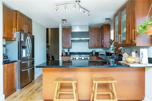 kitchen featuring a kitchen bar, kitchen peninsula, light hardwood / wood-style flooring, and wall chimney range hood