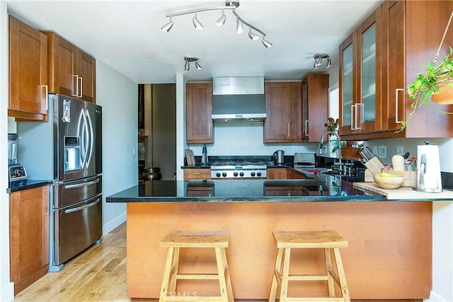 kitchen featuring a sink, stainless steel appliances, dark countertops, wall chimney exhaust hood, and light wood-type flooring