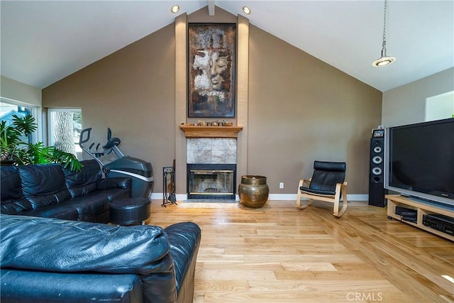 living area with a tiled fireplace, high vaulted ceiling, baseboards, and light wood-style floors